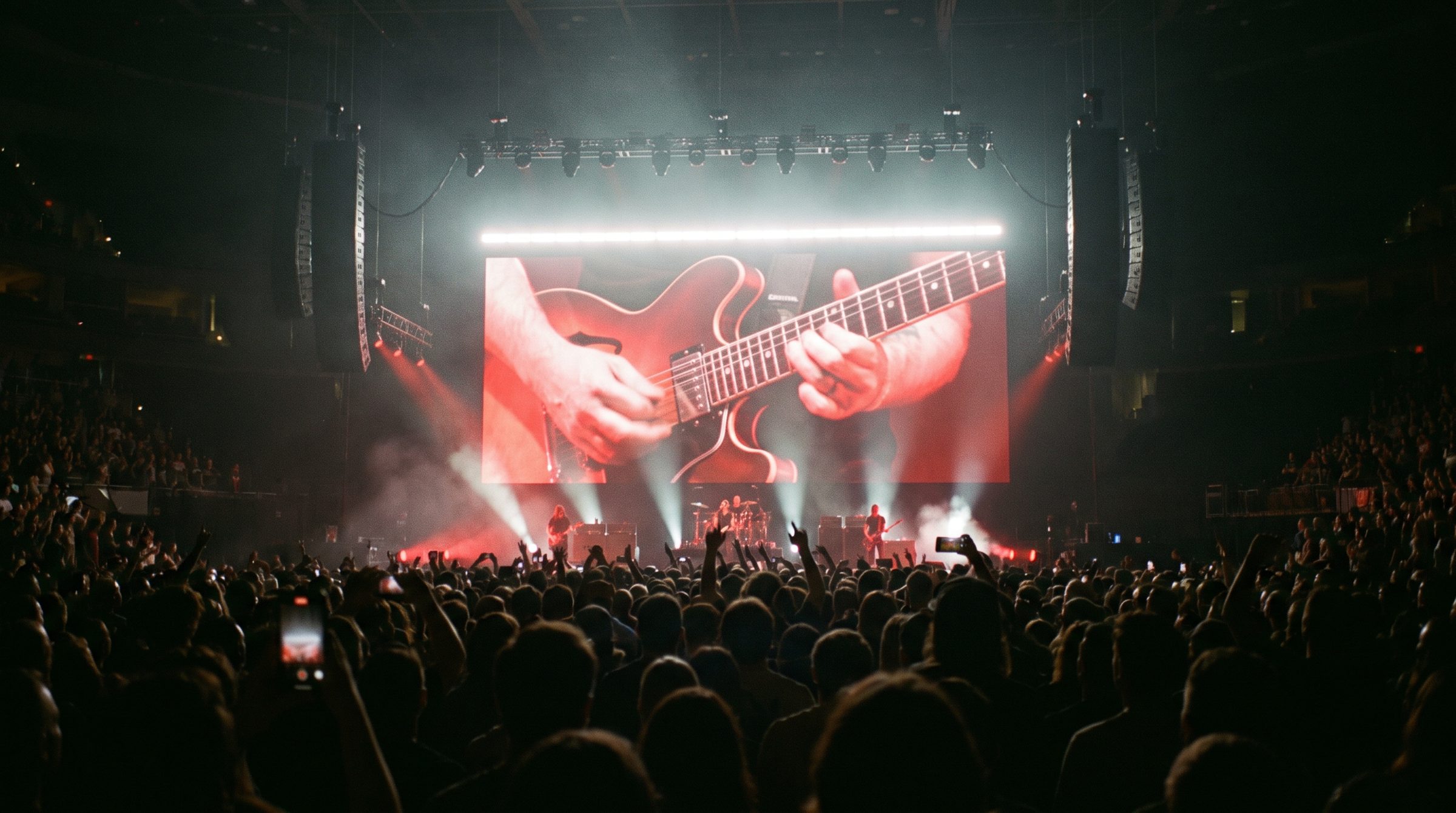 Concert in een volle hal met een LED-wand achter de band en de gitarist live in beeld